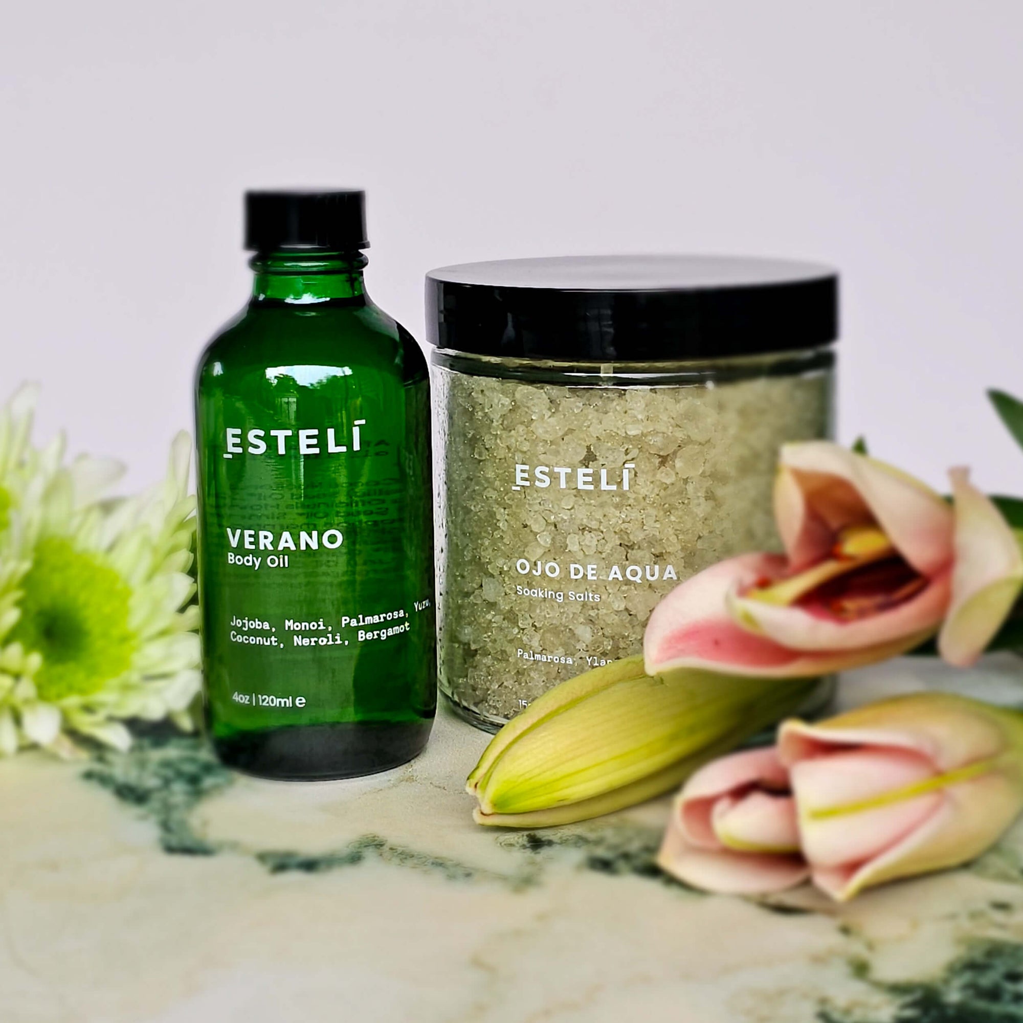 Mothers Day Gift of Esteli Verrano Body Oil and Ojo de Agua Bath Salts with flowers on a marble bathroom counter