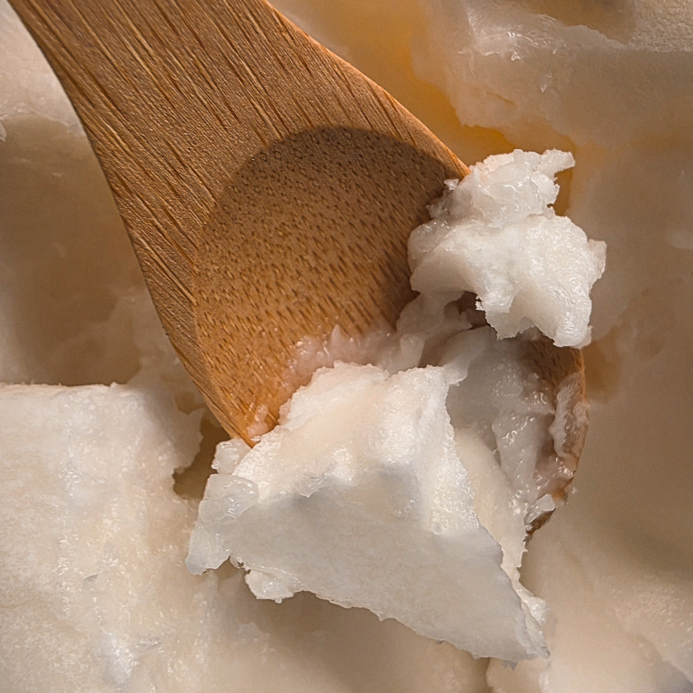 Monoi butter on a wooden spatula, showing its creamy ivory texture.